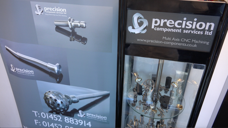 Precision Component Services display stand with machined parts and company contact details