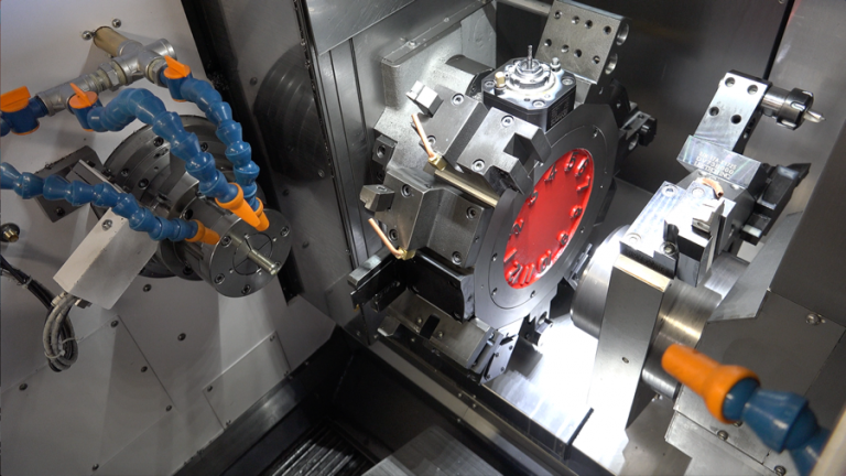 Inside a CNC lathe with coolant hoses and a workpiece lit red